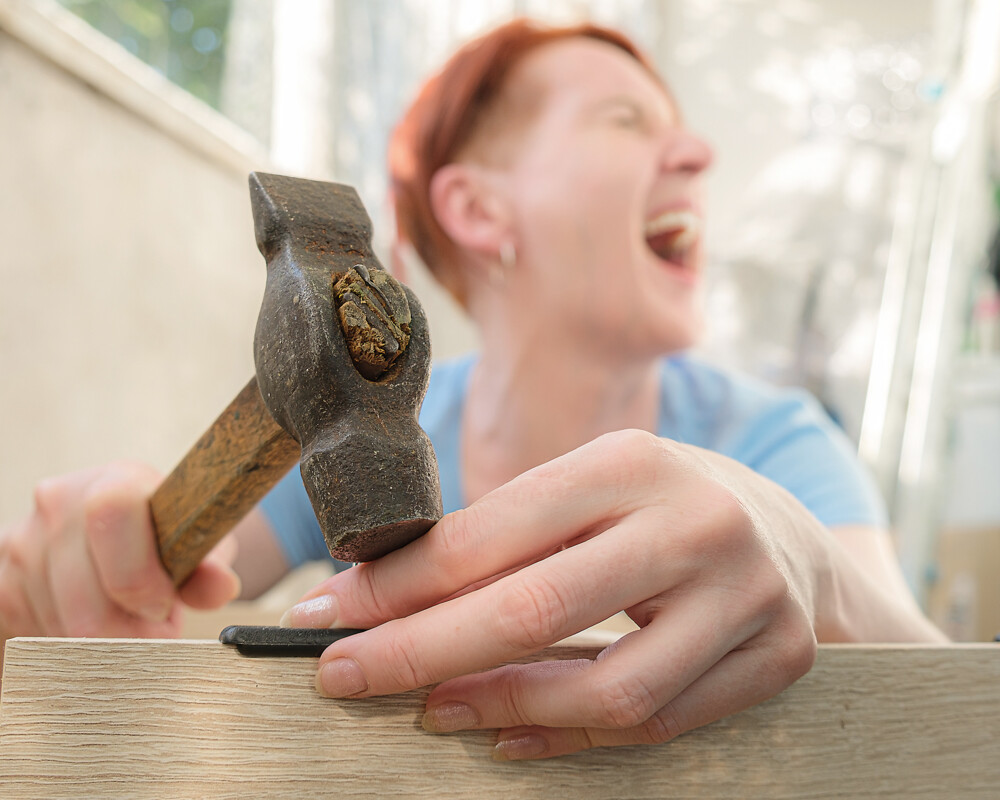 Frau haut sich mit Hammer auf den Finger und schreit.