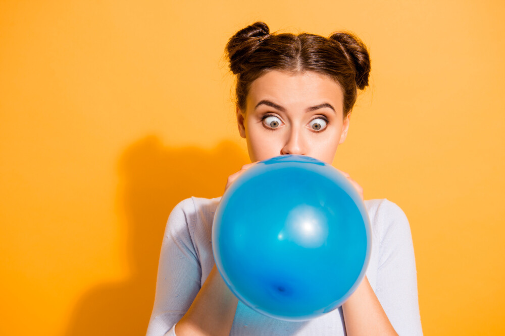 Schielende junge Frau pustet einen blauen Luftballon auf