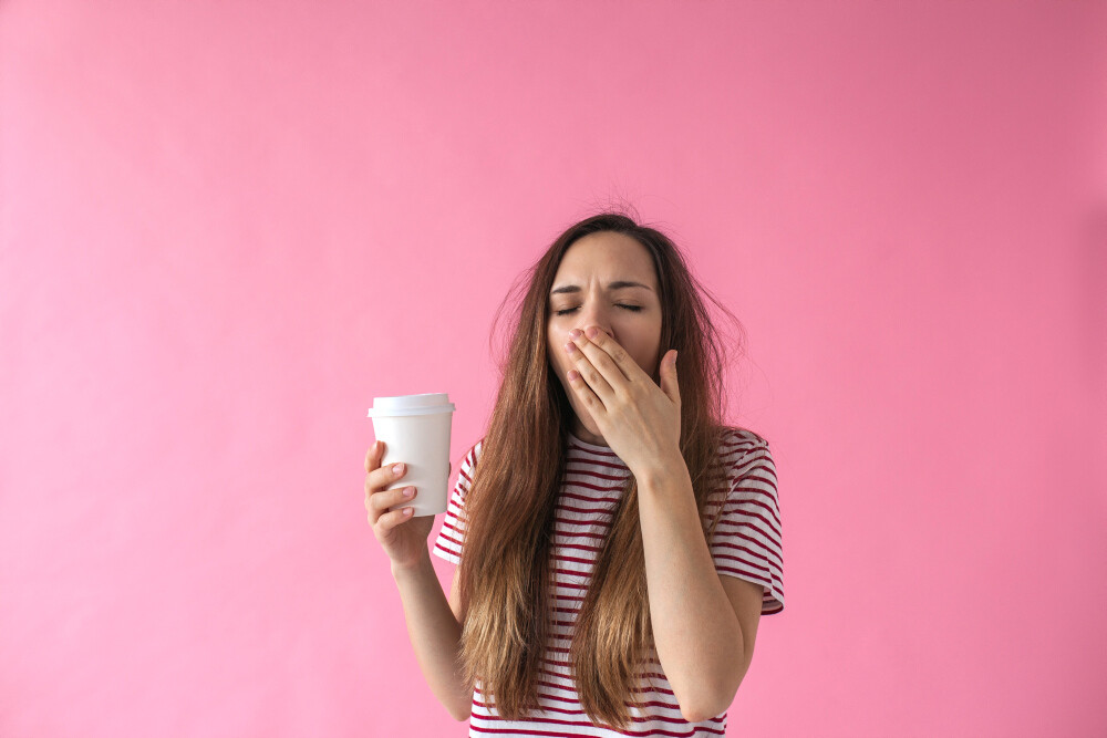 Junge Frau mit Coffee-to-go-Becher in der Hand gähnt