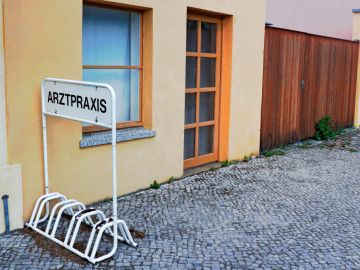 Verlassenes Gebäude mit einem Fahrradständer mit Beschriftung Arztpraxis davor