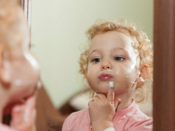 Kleinkind cremt sich vor dem Spiegel ein

